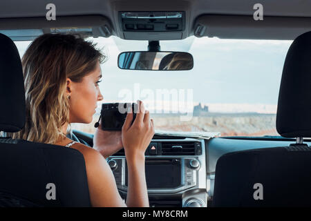 Young woman sitting in vehicle, taking photo through windscreen, using camera, Mexican Hat, Utah, USA Stock Photo