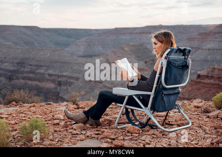 Young woman in remote setting, sitting on camping chair, reading book, Mexican Hat, Utah, USA Stock Photo