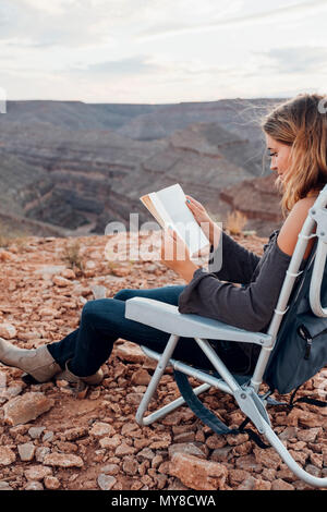 Young woman in remote setting, sitting on camping chair, reading book, Mexican Hat, Utah, USA Stock Photo