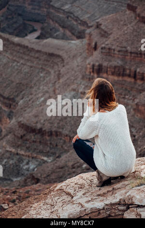 Young woman in remote setting, crouching on rocks, looking at view, rear view, Mexican Hat, Utah, USA Stock Photo