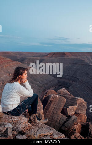 Young woman in remote setting, sitting on rocks, looking at view, Mexican Hat, Utah, USA Stock Photo