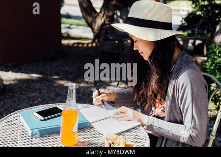 Young woman sitting outdoors, writing in notebook Stock Photo