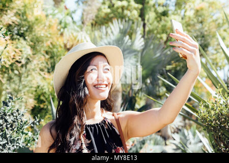 Young woman outdoors, taking selfie in ornamental garden Stock Photo