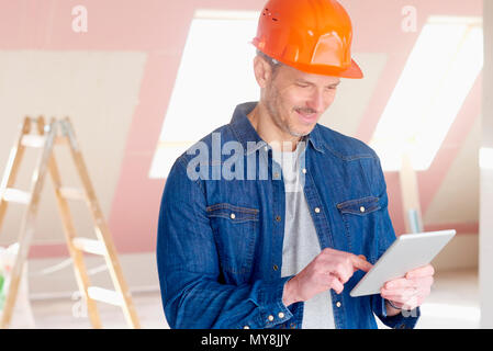 Portrait of middle aged construction worker looking thoughtful while standing at constraction site and using digital tablet. Stock Photo