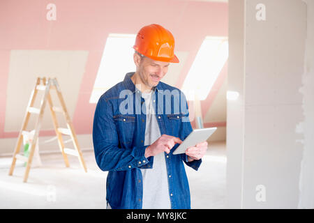 Portrait of middle aged construction worker looking thoughtful while standing at constraction site and using digital tablet. Stock Photo