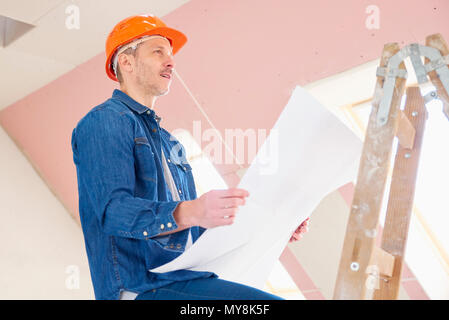 Portrait of construction worker holding plan in his hand while standing on the ladder and working. Stock Photo