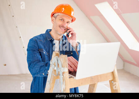 Portrait of happy construction worker using mobile phone and consulting with somebody while using laptop at construction site. Stock Photo