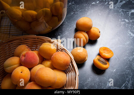 Ripe organic apricots harvested at summer time and big glass jar with canned sweet apricot compote on dark marble. Composition in rustic style - organ Stock Photo