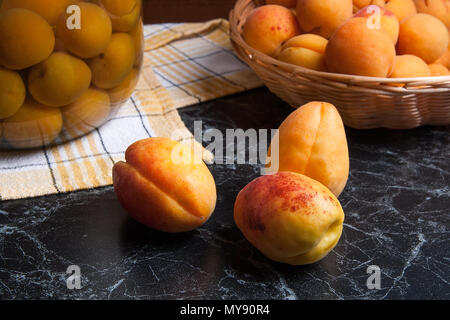 Ripe organic apricots harvested at summer time and big glass jar with canned sweet apricot compote on dark marble. Composition in rustic style - organ Stock Photo