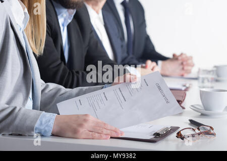 Woman holding CV sittting next to three businesspeople beside table Stock Photo