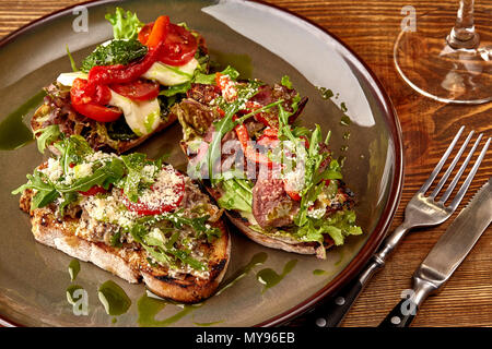 Italian sandwiches - bruschetta with meat pate, arugula, sun dried tomato and seeds on bread on dark wooden table. Stock Photo