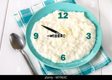 Rice milk porridge with nuts and raisins in a blue dish on a white wooden table. The concept of a breakfast with a clock Stock Photo