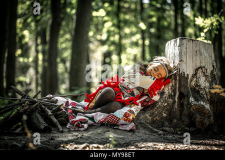 beautiful little girl playing outdoors in Indians ,eating an Apple sitting on a stump Stock Photo