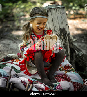 beautiful little girl playing outdoors in Indians ,eating an Apple sitting on a stump Stock Photo