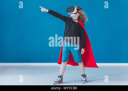 Happy boy dressed up as a superhero feels in the game while using VR glasses Stock Photo