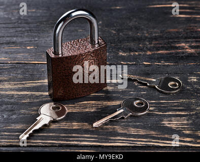 Closed lock with three keys scattered on a dark wooden table Stock Photo