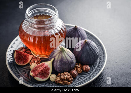 Honey with fresh figs and nuts on slate black background closeup Stock Photo
