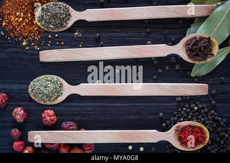 Four wooden spoons with various spices on dark wooden background Stock Photo