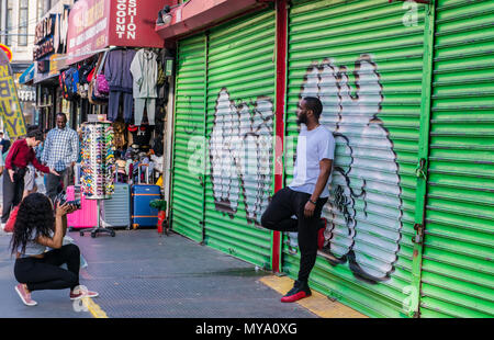 Man leaning against graffiti covered metal shutter, posing for photographer, New York City, USA Stock Photo