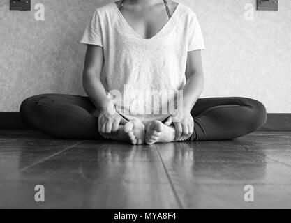 Black and white version of Female dancer sitting down in butterfly pose practicing yoga in the studio Stock Photo