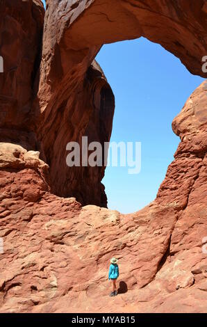Young girl in a blue shirt looking up at Window Arch in Arches National Park, near Moab, Utah. Stock Photo