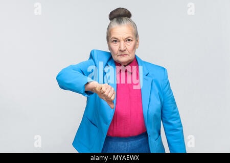 Unhappy woman showing dislike sign. Emotion and feelings, expressive grandmother with light blue suit and pink shirt standing with collected bun gray  Stock Photo
