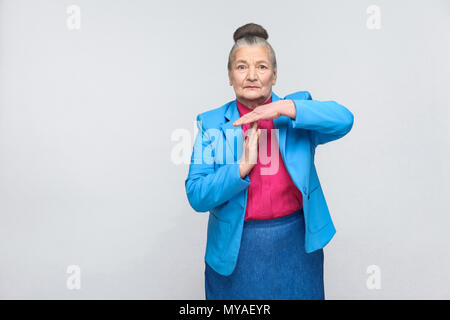 aged woman showing time out sign. Portrait of handsome expressive grandmother with light blue suit and pink shirt standing with collected bun gray hai Stock Photo