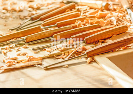 Chisels laid in wooden shavings on the desk. Carving tools lying in the shavings. In a carving workshop. Cutting of linden wood. Stock Photo