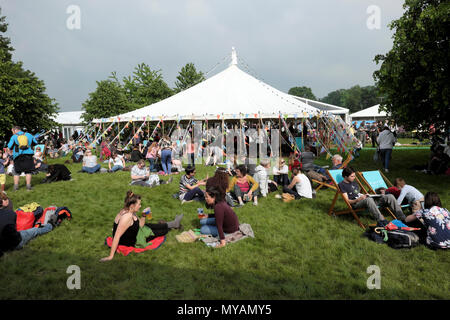 People relaxing sitting and lying on the ground reading outside by marquee on the Hay Festival site in sunshine 2018 Hay-on-Wye Wales UK  KATHY DEWITT Stock Photo