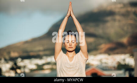 Woman practicing yoga on the terrace of her home. fitness woman meditating in a yoga posture raising her hands and joining both the palms . Stock Photo