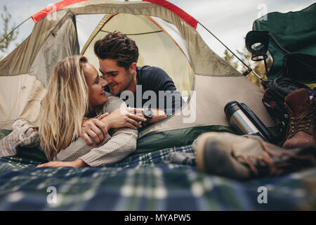 Happy man and woman having a romantic moment in a tent. Couple camping in nature. Stock Photo