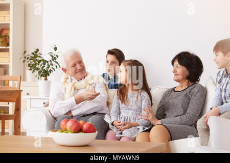 Happy grandparents and grandchildren sitting on a sofa in living room Stock Photo
