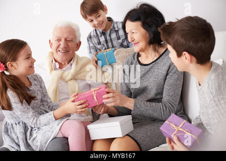 Grandparents and grandchildren sitting on a sofa and exchanging gifts Stock Photo
