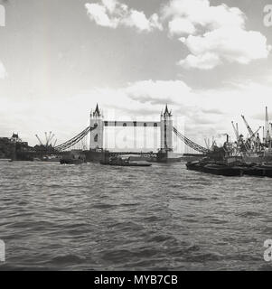 1960s, historical view across the River Thames of the city's iconic Tower Bridge, showing cranes on the riverbank on the right of the picture. In this era, the riverbanks of the Thames began to be developed. Stock Photo