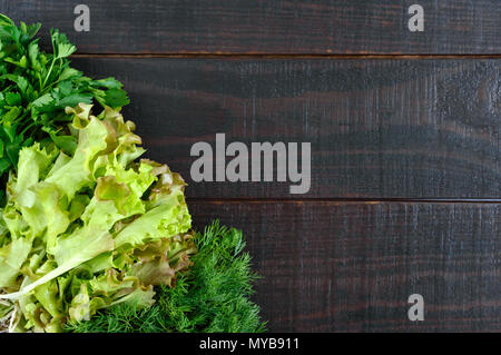 Food background. Lettuce leaves, dill, parsley on a wooden dark background. Fresh greens from the garden. Free space for an inscription. Stock Photo