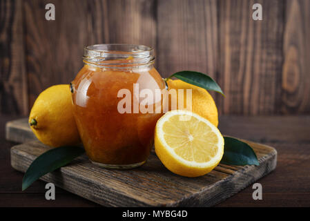 Lemon jam in jar with fresh lemons on wooden background closeup Stock Photo