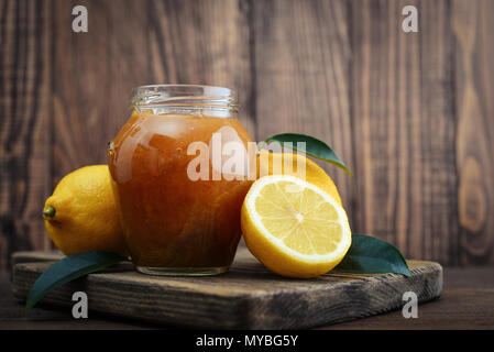 Lemon jam in jar with fresh lemons on wooden background closeup Stock Photo