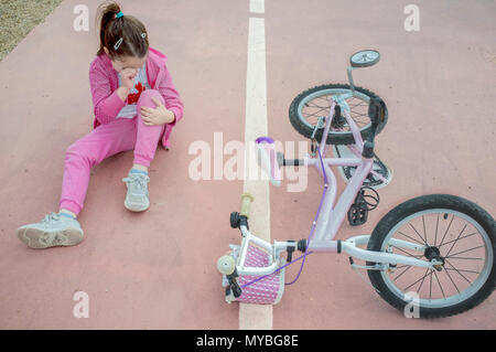 Child girl crying after bike accident. Pink female bike on floor with training wheels Stock Photo