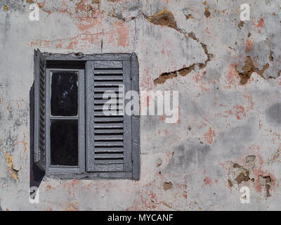 Window with gray wooden vintage frames and sashes on the old wall of the house with spots and cracks. Stock Photo