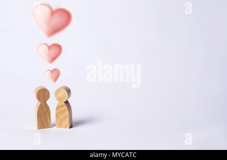 Two wooden figures of people stand together on a white background with hearts over their heads. Concept of love, couple, young people. Minimalism. Rom Stock Photo