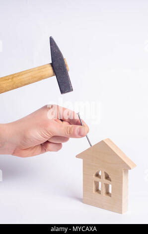 Man hammers a nail with a hammer in a miniature wooden house on a white background. Concept of repair of houses. The worker conducts repair work at th Stock Photo