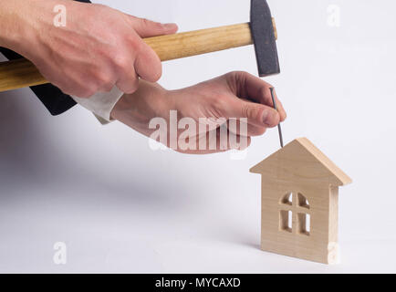 Man hammers a nail with a hammer in a miniature wooden house on a white background. Concept of repair of houses. The worker conducts repair work at th Stock Photo