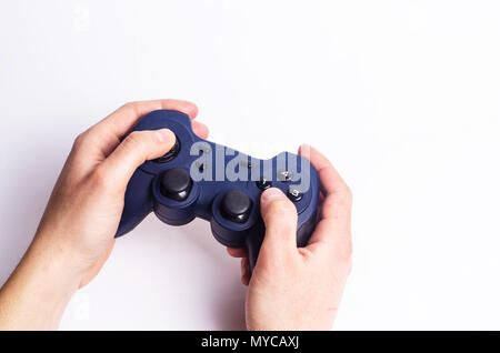 A young guy holds a joystick and plays computer games on a white background. Blue joystick in the hands of man. The concept of computer games and ente Stock Photo