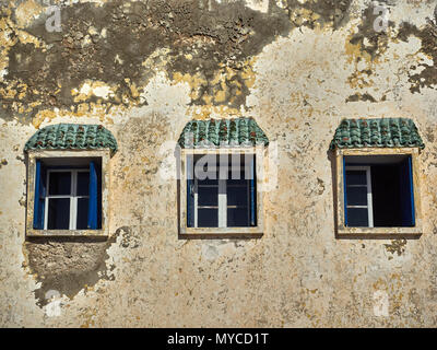 Three vintage windows with white wooden frames on the wall of an old house, with water and mildew, over the windows of the visor with green tiles. Stock Photo