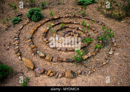 Stone spiral made up of lots of individual rocks on a dry stony floor with green plants growing up through the spiral of stones. Stock Photo