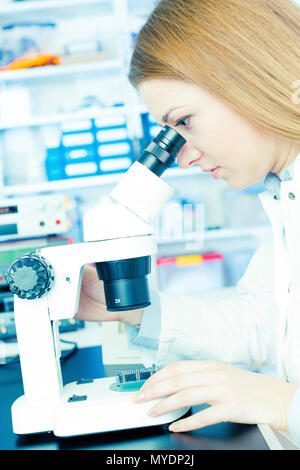Technician using microscope to examine microelectronics. Stock Photo