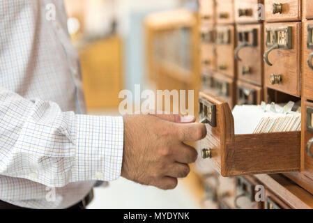 A man opens wooden cabinet stored library index. Stock Photo