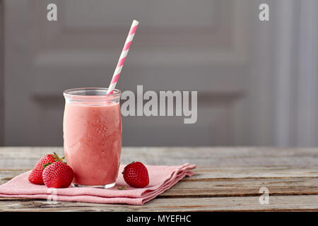 Yogurt and strawberry smoothie in jar with drinking straw on wooden table Stock Photo