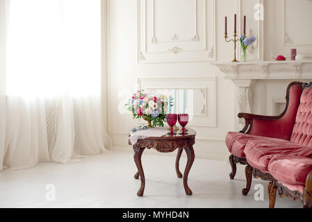 Decorated vintage table in white baroque style interior with red luxury sofa. Table is set for romantic event. Stock Photo