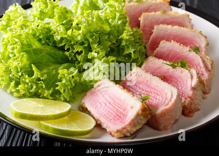 seared ahi tuna in breading with lettuce and lime closeup on a plate on a black table. horizontal Stock Photo